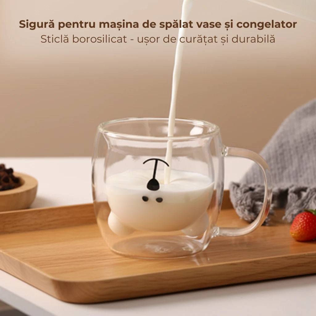 Cana in forma de ursulet, sta pe o tava din lemn, pe o masa alba. Se toarna lapte in cana. Textul prezent in poza: Sigura pentru masina de spalat vase si congelator. Sticla borosilicat - usor de curatat si durabila.
