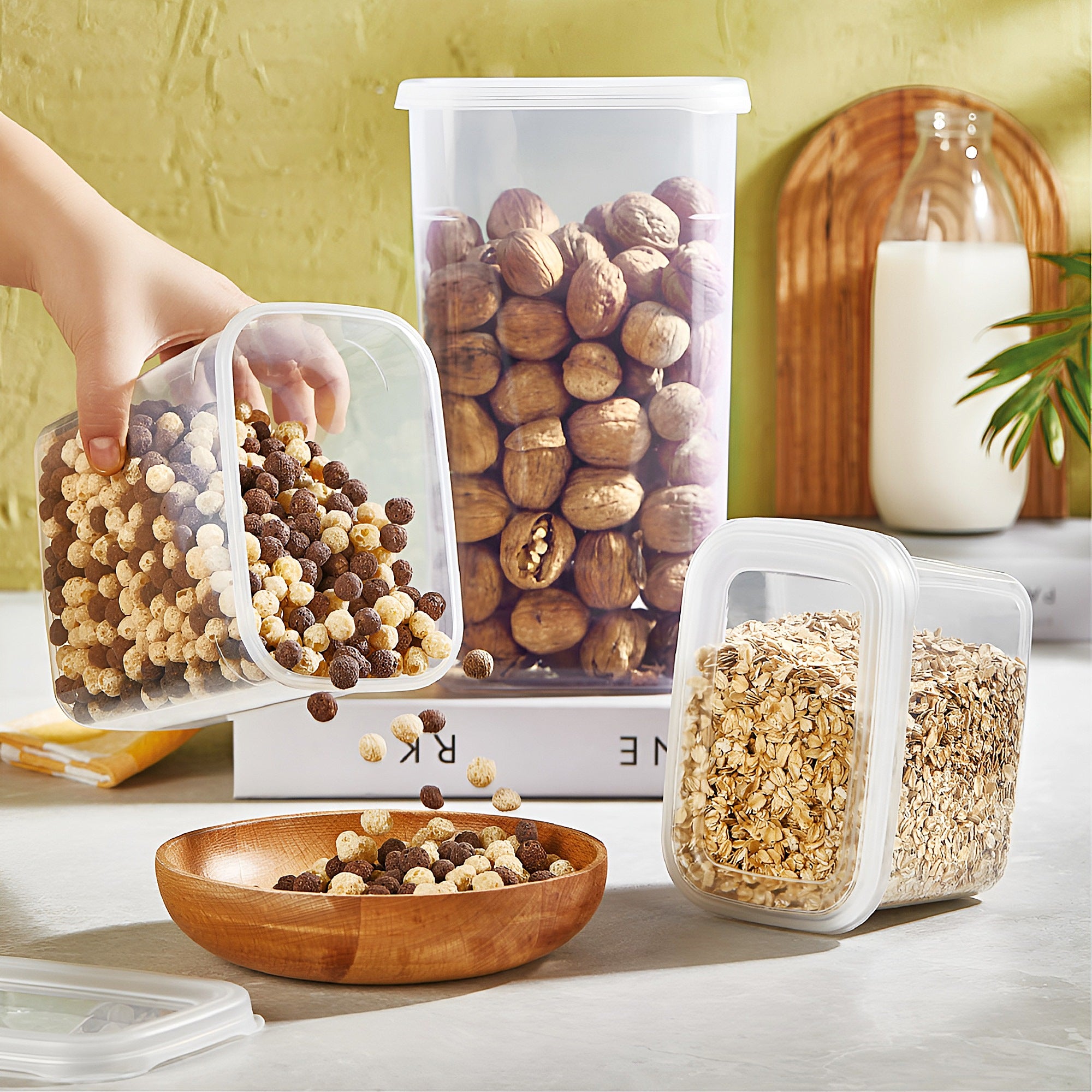 # recipiente din set Koken pe masa. O mana de copil pune cereale dintr-un recipient intr-o farfurie.